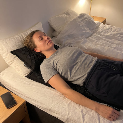 Kvinde slapper af på SleepMat akupressurmåtte med pude før sengetid